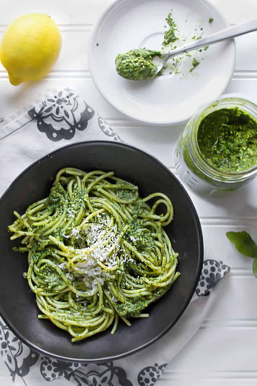 arugula pesto in a black bowl with a lemon on the side and jar of pesto