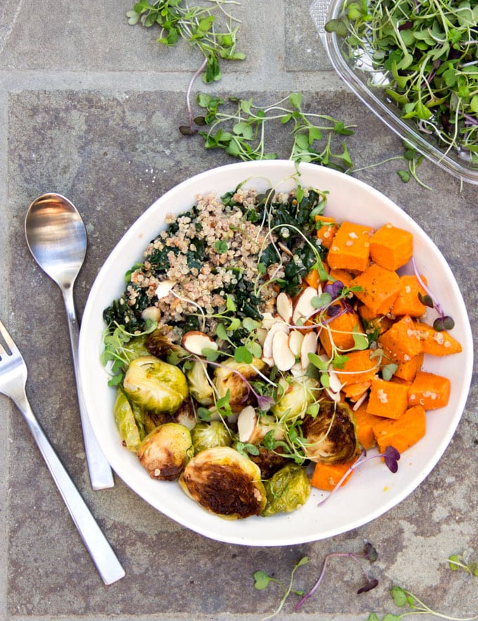 A buddha bowl on a green cloth napkin: A sweet potato Brussels sprouts buddha bowl with quinoa, wilted kale and a sprinkle of slivered almond and micro greens