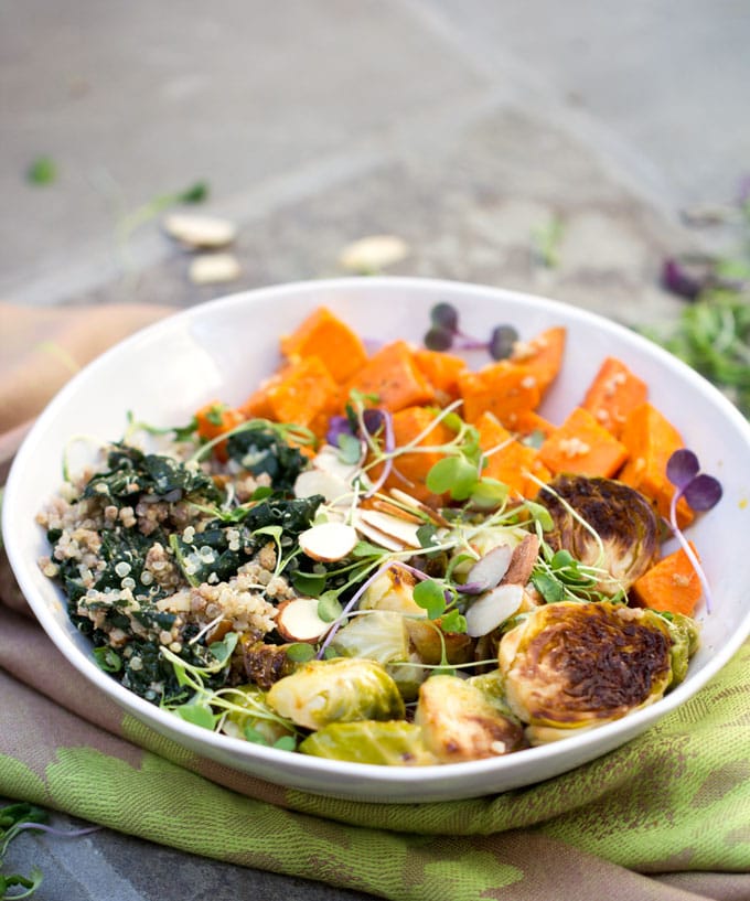 A sweet potato brussels sprout buddha bowl with roasted vegetables kale, quinoa, lemon dressing and a garnish of slivered almonds 