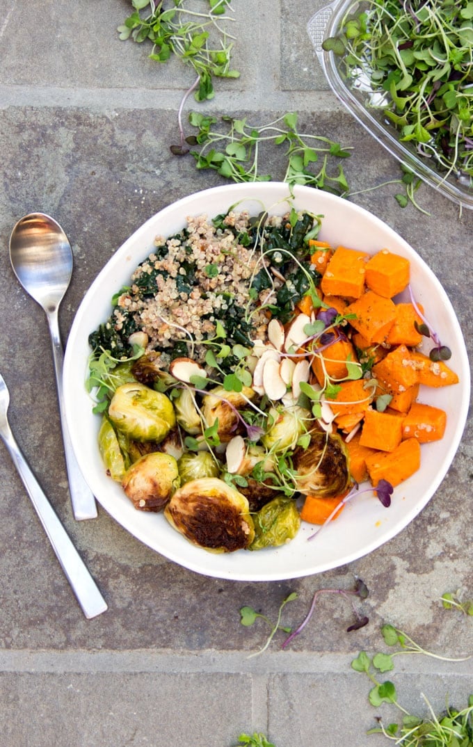 A buddha bowl on a green cloth napkin: A sweet potato Brussels sprouts buddha bowl with quinoa, wilted kale and a sprinkle of slivered almond and micro greens