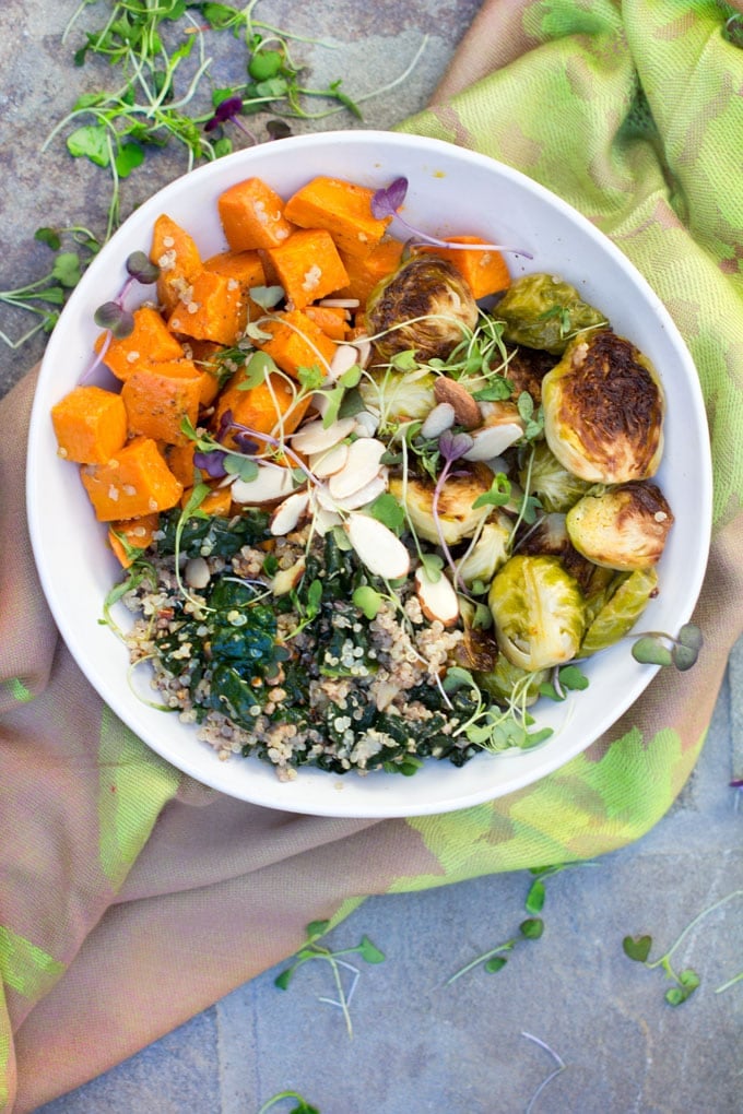 A buddha bowl on a green cloth napkin: A sweet potato Brussels sprouts buddha bowl with quinoa, wilted kale and a sprinkle of slivered almond and micro greens