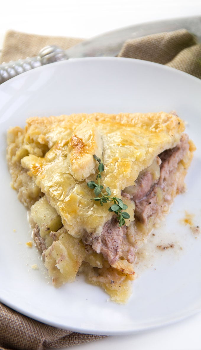 close up overhead picture of a slice of pork pie on a white plate with a thyme sprig on top