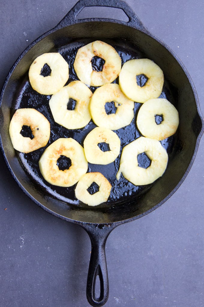 11 thinly sliced apple rings spread out in the bottom of a cast iron skillet