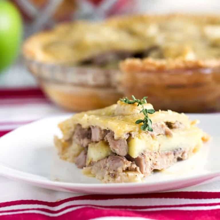 Slice of pork pie on a plate with the whole pie in the background.