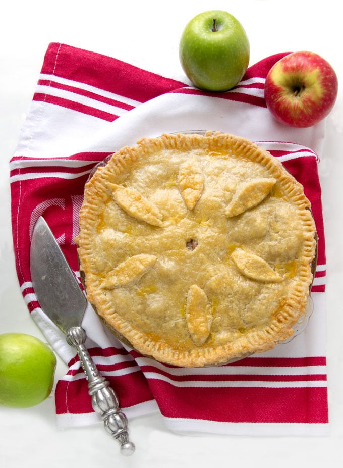 overhead shot of a whole cheshire pork pie on a red and white striped dish towel surrounded by two green apples and one red apple and a pie serving knife