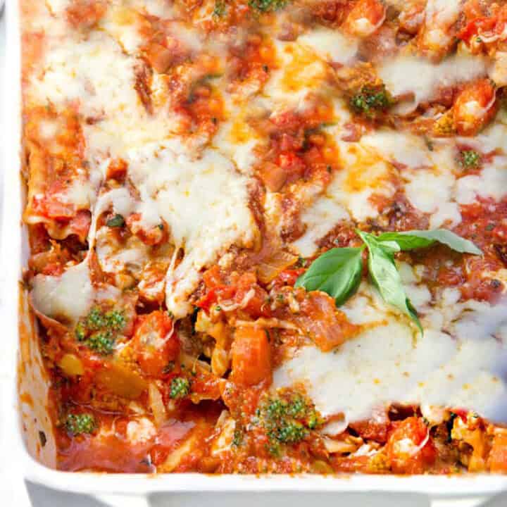 roasted vegetable lasagna in a porcelain roasting pan topped with a sprig of basil.