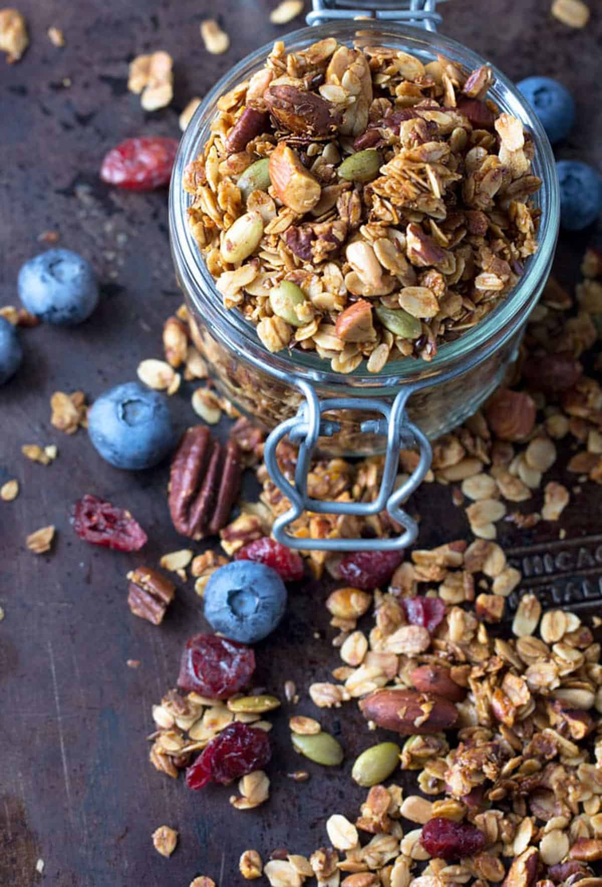 uncovered mason jar brimming and overflowing with nut and seed granola plus a few blueberries scattered around.