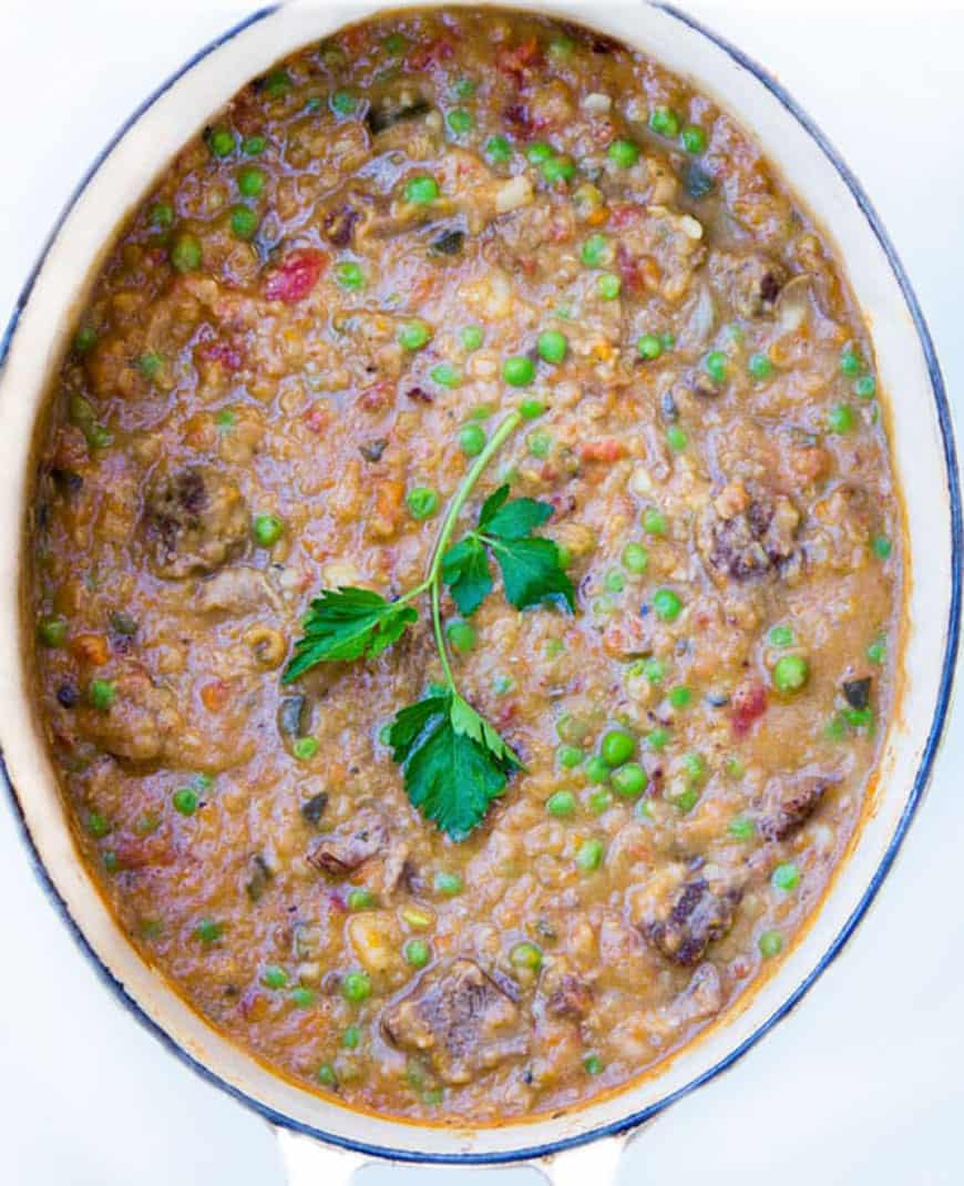 overhead shot of a white oval Dutch oven filled with minestrone soup with beef, a lovely parsley sprig in the middle