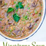 Pinterest pin showing an overhead view of an oval dutch oven filled with minestrone soup, with a large sprig of parsley in the center