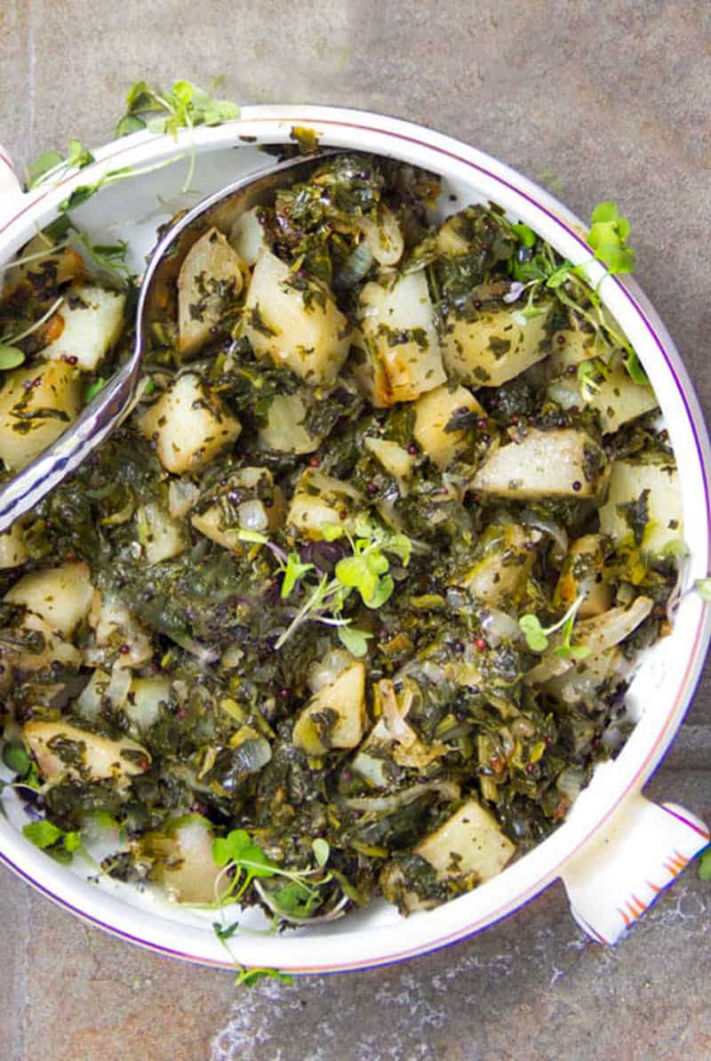 a white casserole filled with Indian Saag Aloo - spinach and potatoes