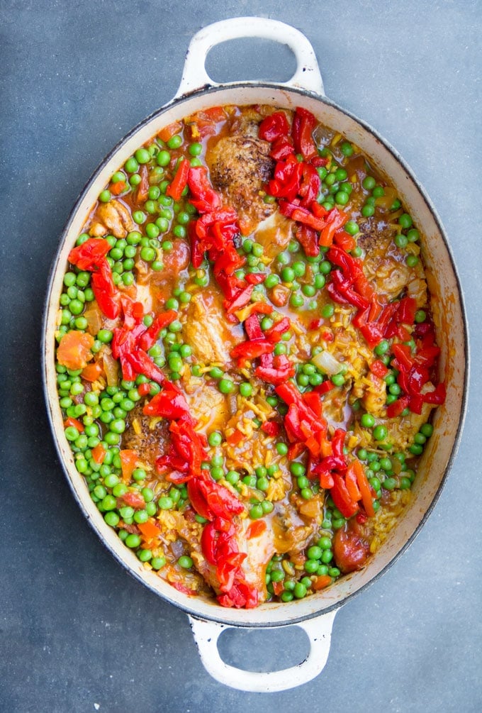 Overhead shot of a white oval Dutch oven filled with colorful Arroz Con Pollo, Spanish chicken and rice casserole.