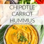 a bowl of orange colored chipotle carrot hummus seen from above with crudites and pita chips on the side