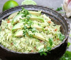 a dark metal bowl filled with Venezuelan avocado chicken salad garnished with 3 slices of avocado and chopped cilantroa dark metal bowl filled with Venezuelan avocado chicken salad garnished with 3 slices of avocado and chopped cilantro