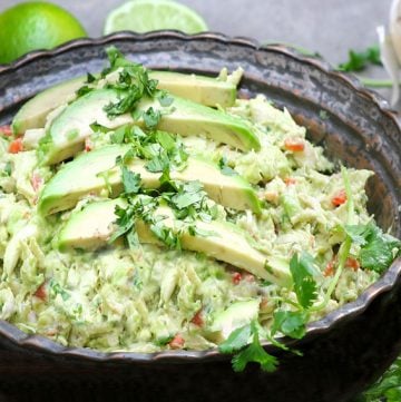 a dark metal bowl filled with Venezuelan avocado chicken salad garnished with 3 slices of avocado and chopped cilantroa dark metal bowl filled with Venezuelan avocado chicken salad garnished with 3 slices of avocado and chopped cilantro