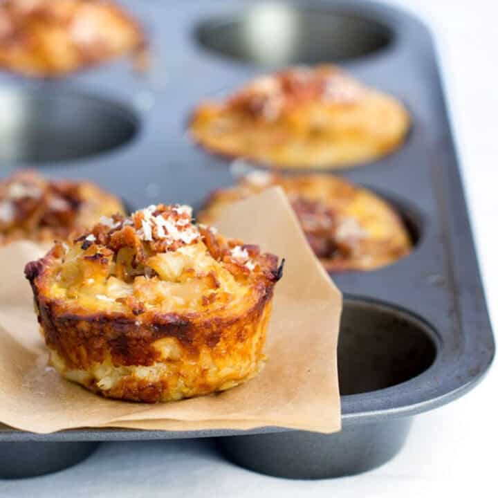 muffin tin with mini savory cauliflower tarts. One tart on a small square of parchment paper on the top of the muffin tin.