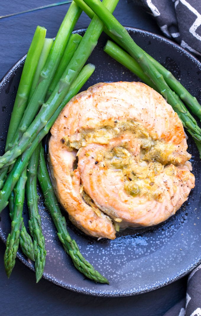 a black plate topped with a stuffed salmon roulade surrounded by steamed asparagus