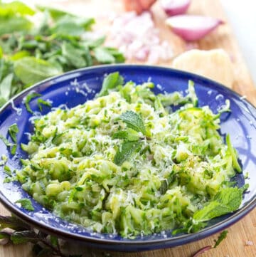 Blue bowl filled with sautéed shredded zucchini. A mint leaf on top.