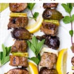 Pinterest pin: two kebabs with hunks of grilled lamb and figs, lemon slices and mint sprigs strewn around