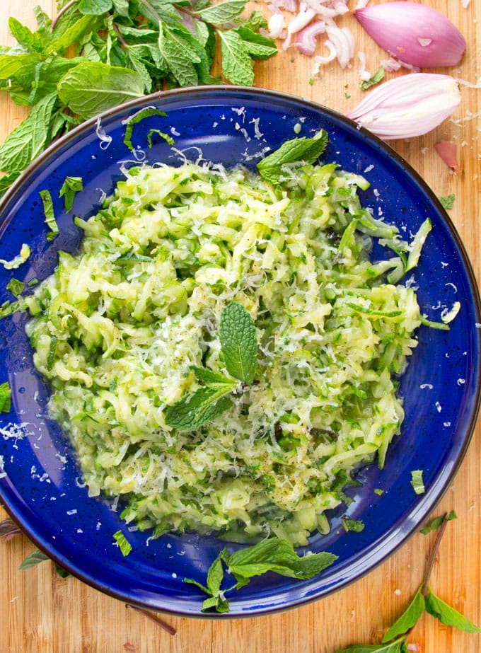 close up of a blue bowl filled with sautéed shredded zucchini, parmesan and mint leaves.