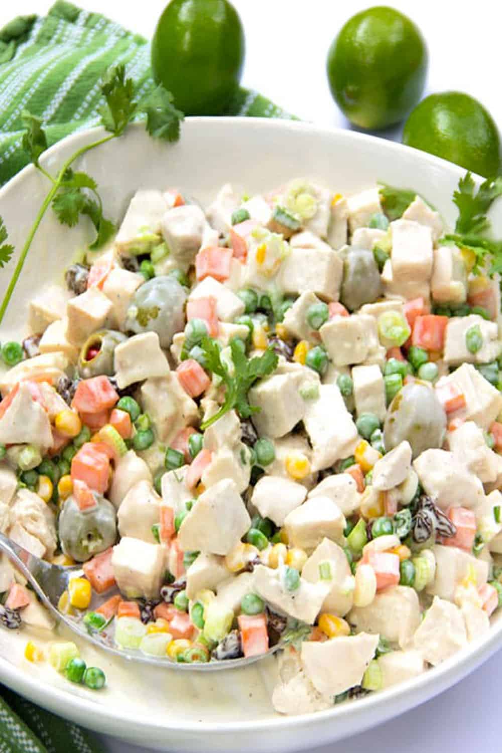 white bowl filled with colorful Brazilian chicken salad that has peas, corn, carrots, olives and raisins
