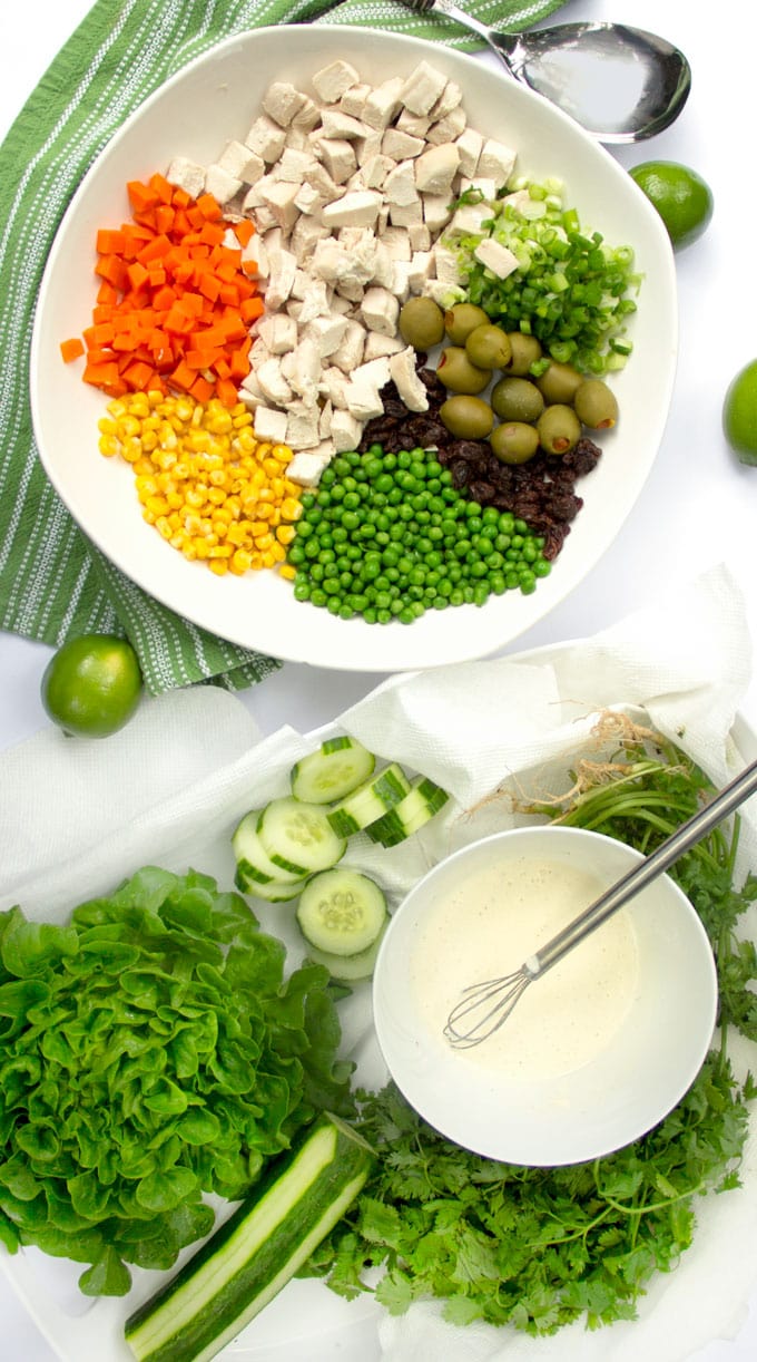 Overhead shot of all the Salpicao ingredients in a white bowl: cubed chicken, chopped carrots, corn, peas, raisins, olives and scallions