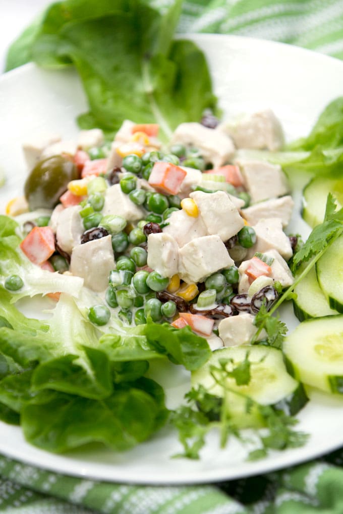 A white plate topped with colorful Brazilian Chicken salad: Salpicao, with cubes of poached chicken, carrots, peas, raising and olives, tossed with creamy lime dressing