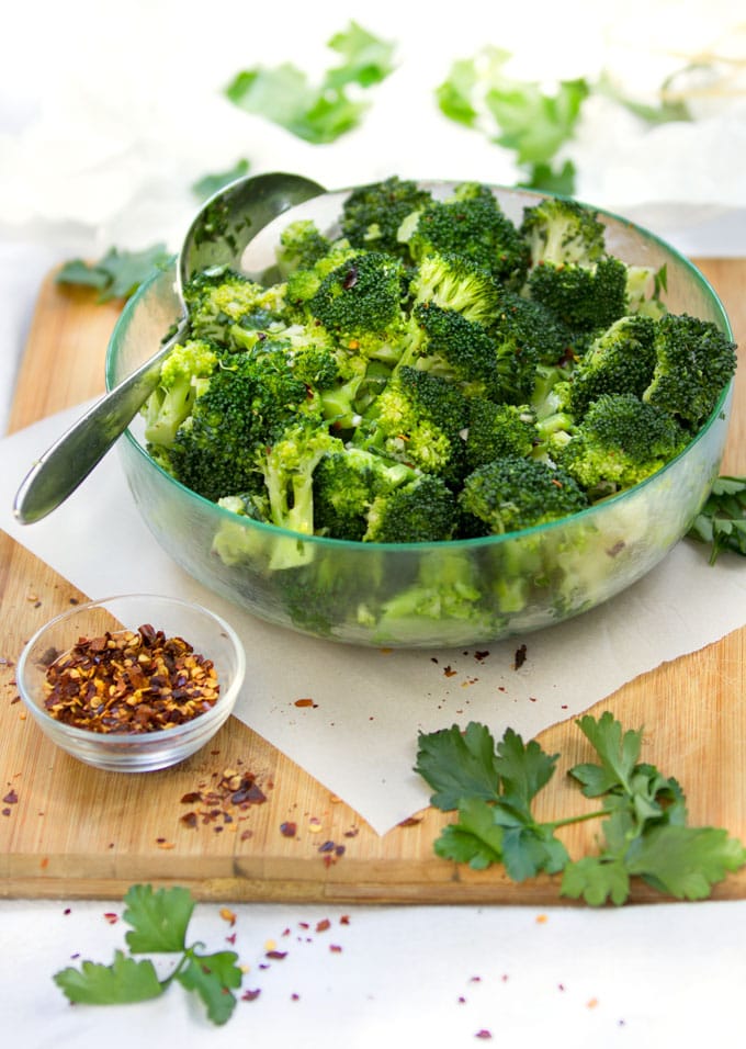 chimichurri broccoli salad in a bowl with a small bowl of crushed red pepper and some parsley leaves