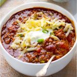 bowl of award winning chili con carne topped with shredded cheese and sour cream