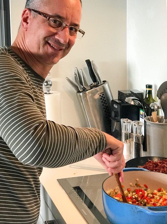 Ed Goldfinger standing over a pot of chili, stirring it with a wooden spoon.
