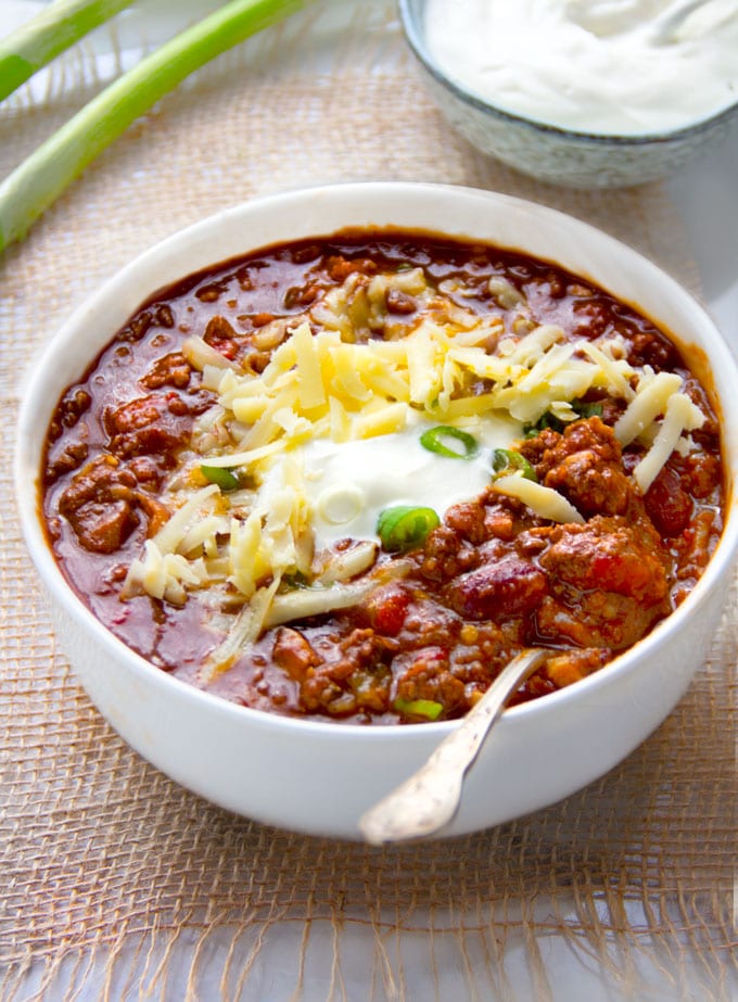 a bowl of award winning chili con carne topped with shredded cheese, sour cream and scallions.