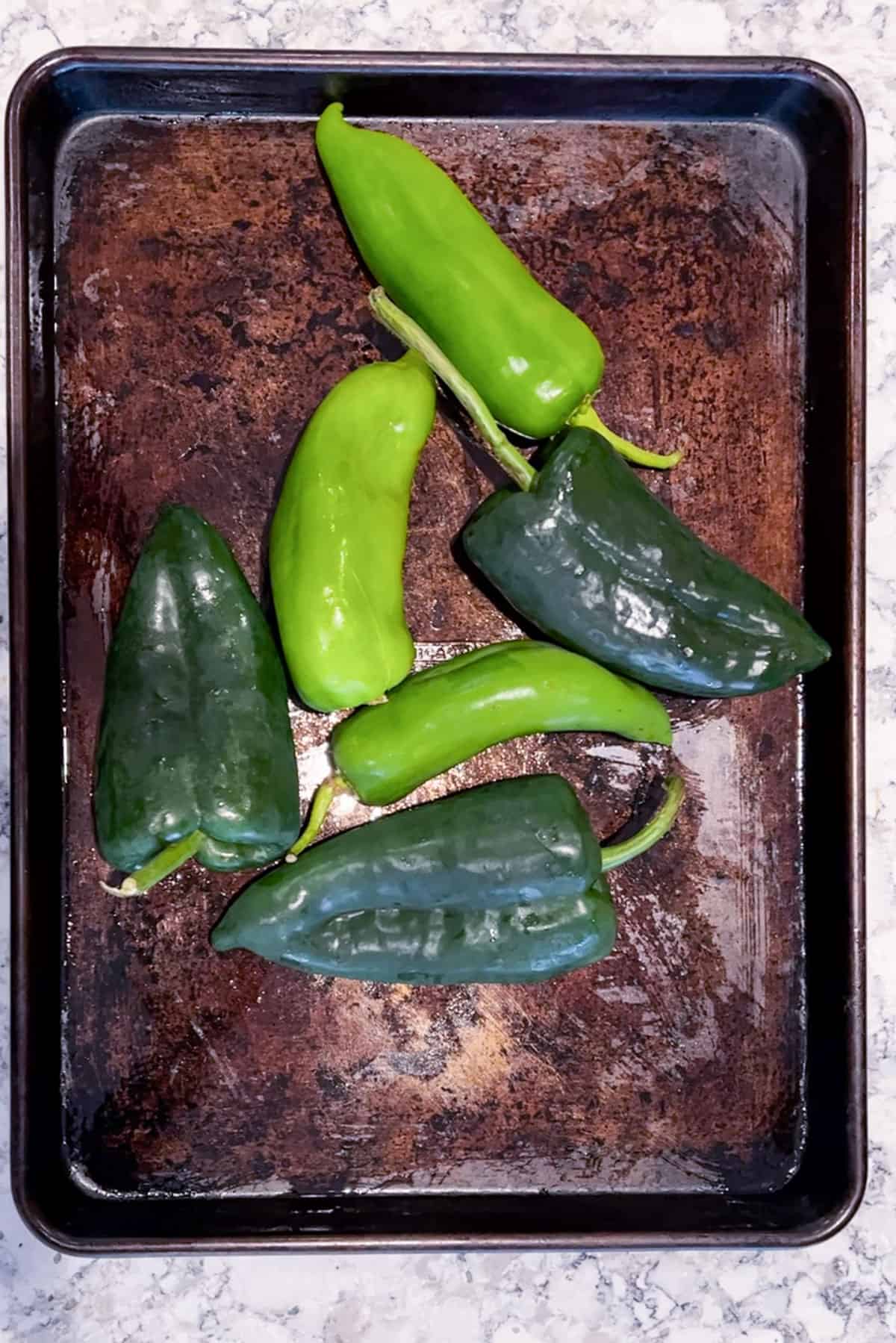 3 Anaheim chilies and 3 poblano chilies on a rimmed baking sheet.
