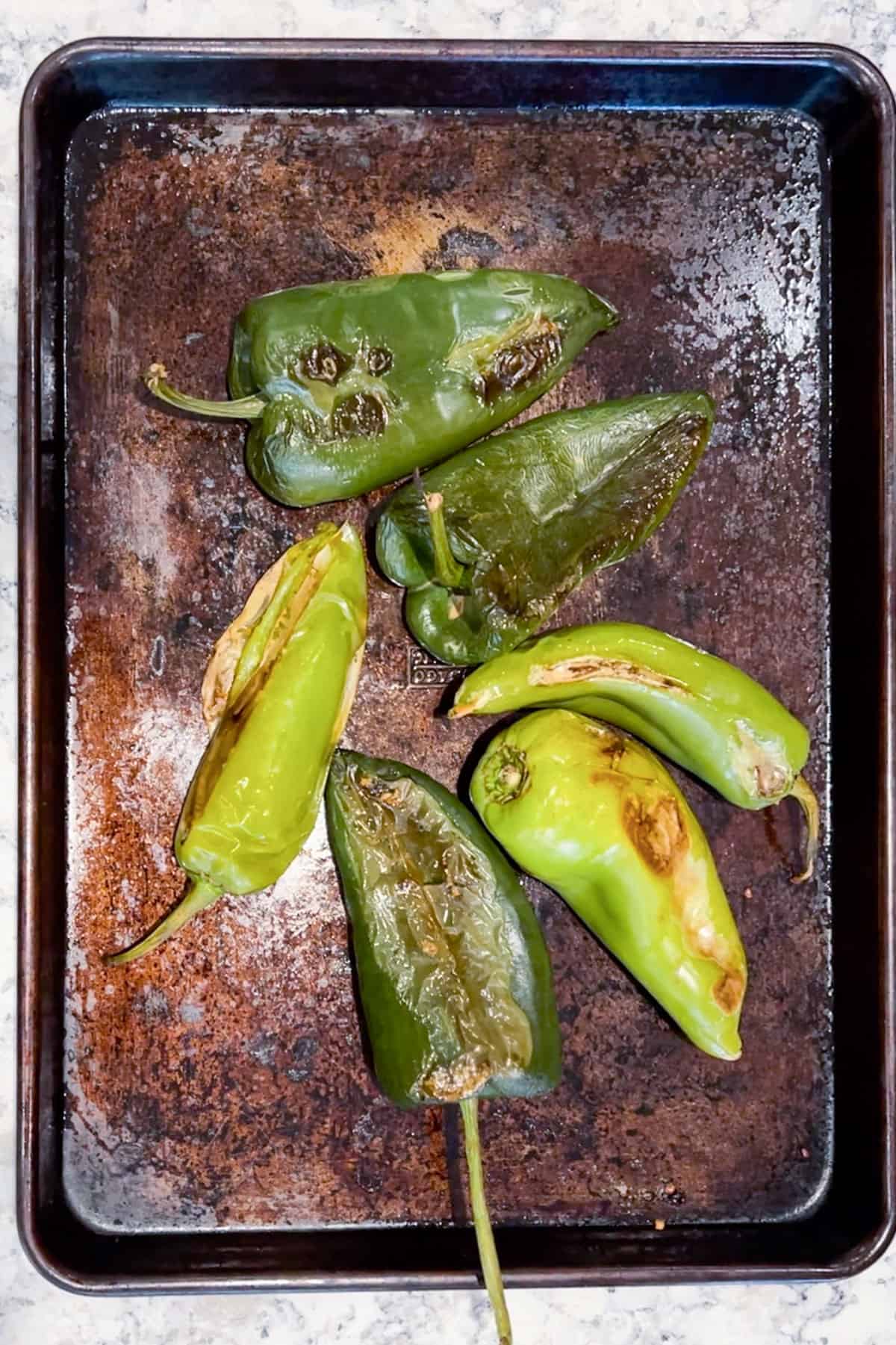 3 roasted Anaheim chilies and 3 roasted poblano chilies on a rimmed baking sheet.