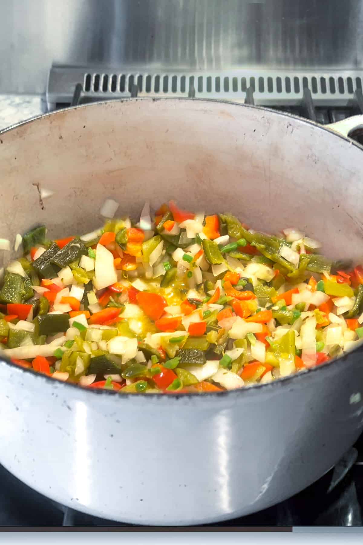 Dutch oven filled with chopped onions, bell peppers, roasted chili peppers and garlic, sauteeing.