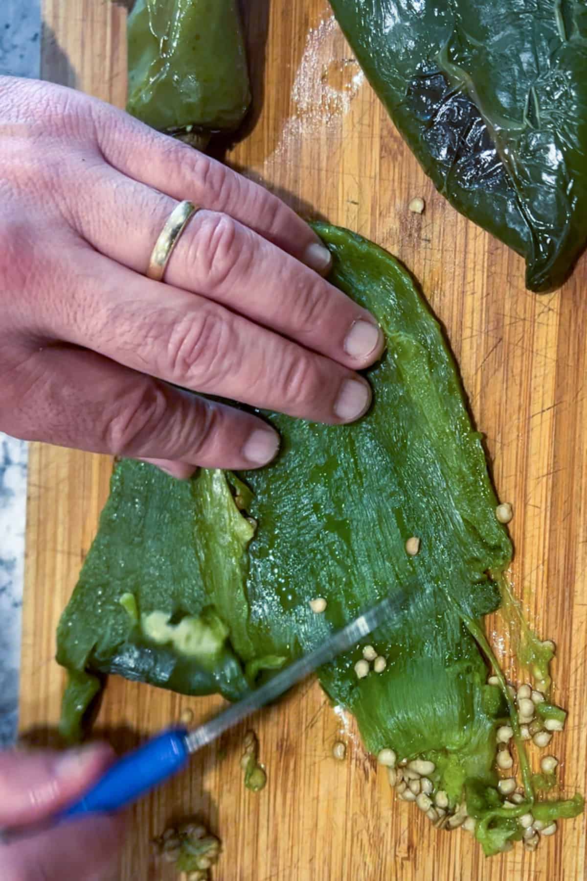 A hand holding a peeled roasted poblano chili and using a small knife to scrape the seeds out.