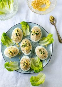 6 French Deviled Eggs Mimosa on a light blue plate, decorated with small lettuce leaves.