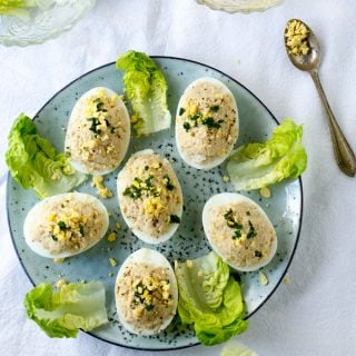 6 French Deviled Eggs Mimosa on a light blue plate, decorated with small lettuce leaves.