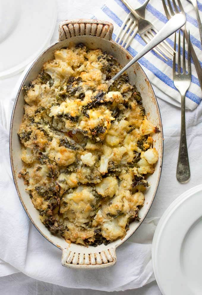 a casserole filled with cheesy cauliflower kale quinoa casserole, with lots of forks next to it on a blue and white striped napkin