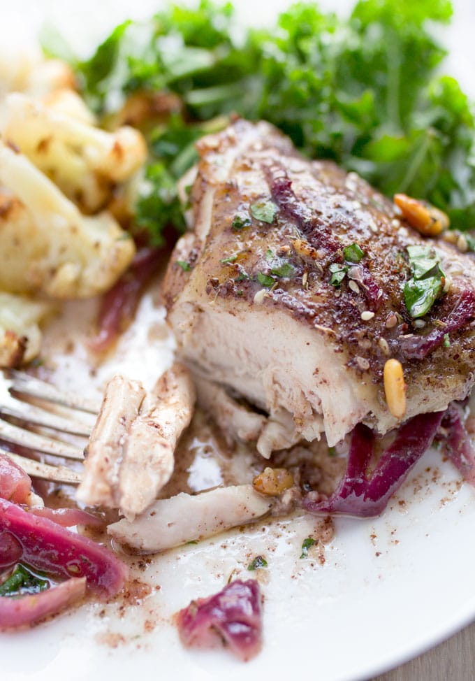 close up of a white plate with one chicken thigh, sliced, with a forkful and some veggies