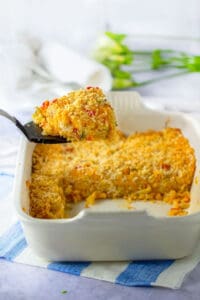 funeral potatoes in a white casserole dish with a large scoop of it on a spatula that is help up above the casserole dish