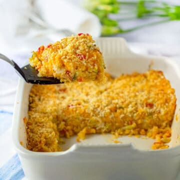 funeral potatoes in a white casserole dish with a large scoop of it on a spatula that is help up above the casserole dish