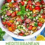 Pinterest pin: close up overhead shot of a white serving bowl filled with a colorful salad of sliced cherry tomatoes, chickpeas, cubed feta, chopped cucumbers, and mint leaves