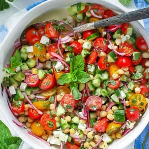 Mediterranean chickpea salad with tomatoes, cucumbers and mint, in a serving bowl with a serving spoon.