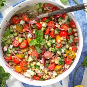 Mediterranean chickpea salad with tomatoes, mint, feta, cucumbers and chickpeas in a serving bowl with a serving spoon.