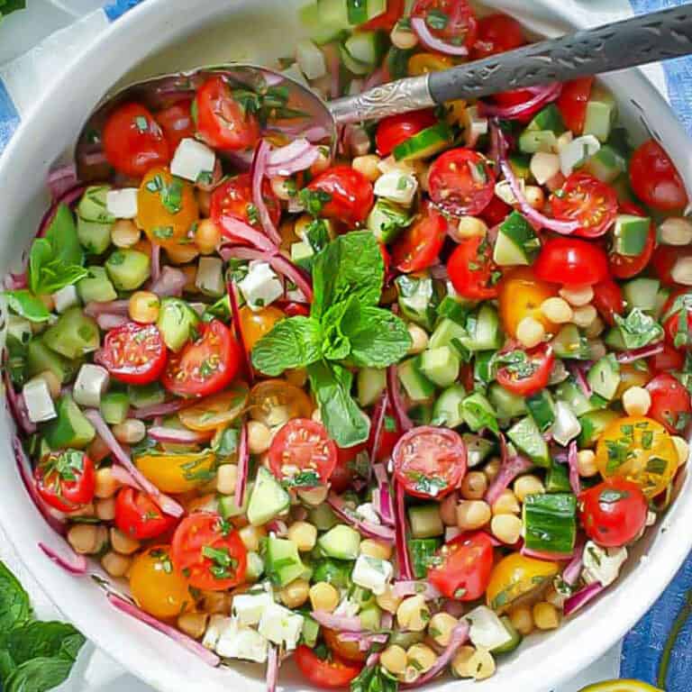Mediterranean chickpea salad with tomatoes, mint, feta, cucumbers and chickpeas in a serving bowl with a serving spoon.