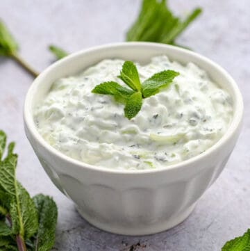 white bowl filled with cucumber raita and garnished with a sprig of fresh mint