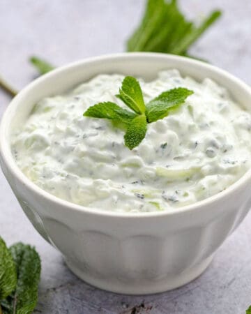 white bowl filled with cucumber raita and garnished with a sprig of fresh mint