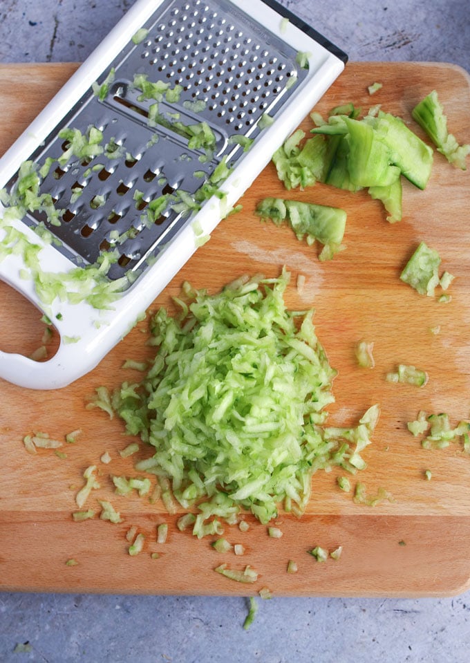 grated cucumber on a blond wood cutting board with a rectangular grater