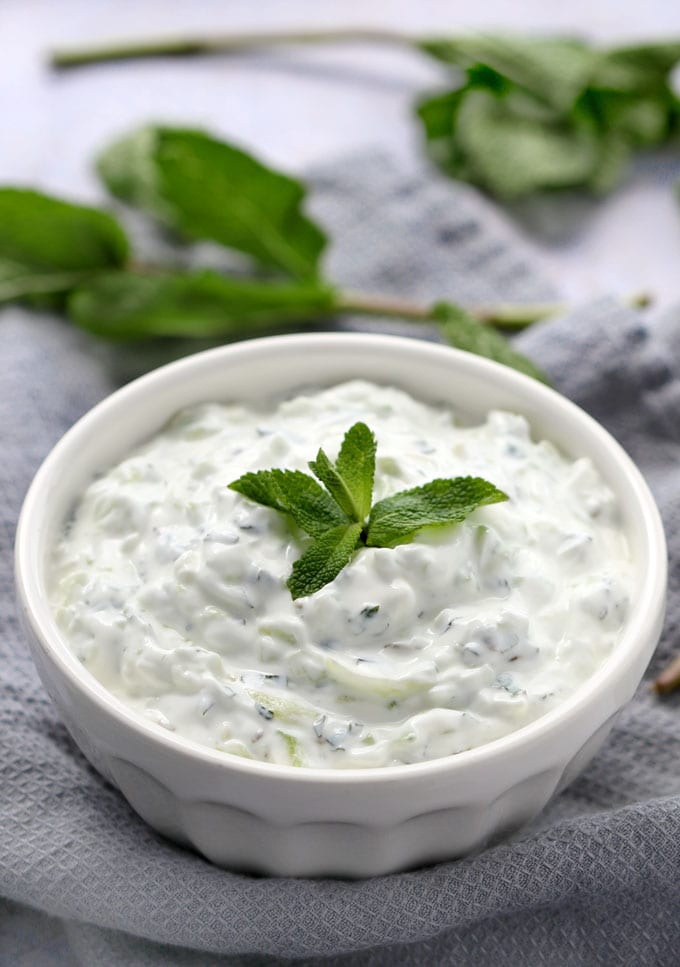 white bowl filled with cucumber raita with a garnish sprig of mint in the center