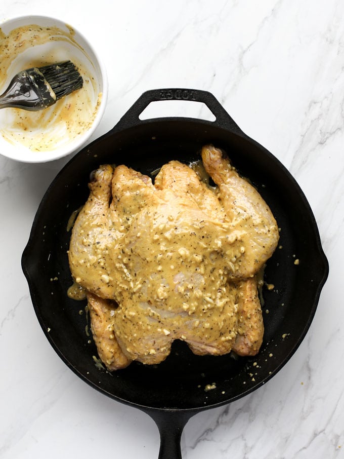 butterflied chicken in a cast iron skillet topped with mustard garlic mixture