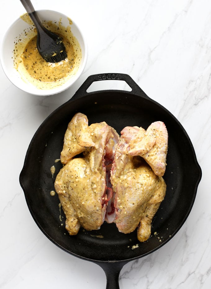 whole butterflied chicken in a skillet with mustard garlic mixture
